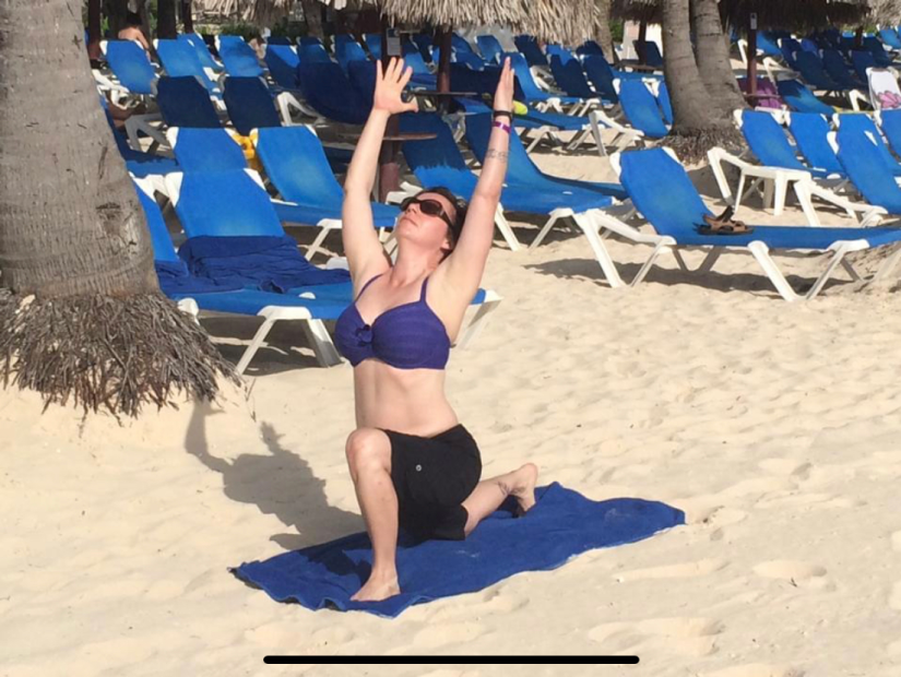 Deb in Warrior one pose on top of her mat in the sands of a beach in Punta Cana.